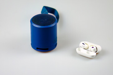 Blue Portable Speaker and White Wireless Earbuds on Light Surface
