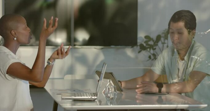 African American woman and Asian man discussing work at office table with laptops