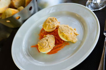 Several boiled chicken eggs with meat filling are laid out on plate. Snack is on top of salad of grated fresh carrots.