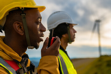 Two engineers wearing safety helmets and vests are using a walkie talkie to communicate, with a...
