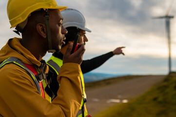 Two engineers working at a wind turbine farm, one pointing and the other using a walkie talkie to communicate