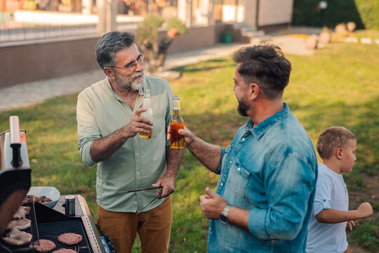 Family enjoying barbecue and toasting with beer bottles in garden