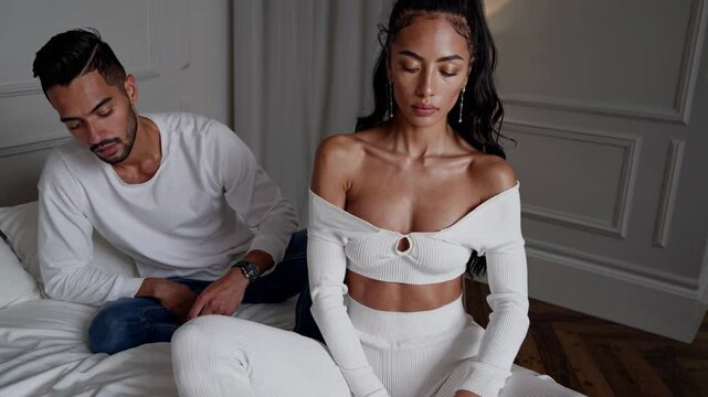 Una mujer con expresi&oacute;n seria mira a c&aacute;mara mientras un hombre, sentado detr&aacute;s, desv&iacute;a la mirada. Ambos en un entorno &iacute;ntimo y elegante, con tensi&oacute;n emocional sutil.  