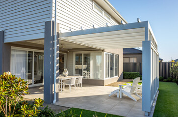 A contemporary residential backyard patio with a covered pergola attached to a modern home. Outdoor...