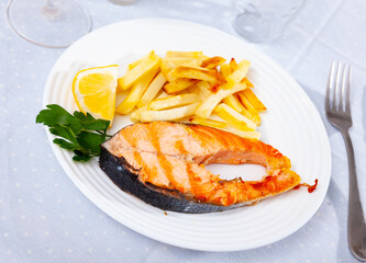 Appetizing grilled salmon steak with side dish of French fries served with slice of lemon and fresh parsley sprig..