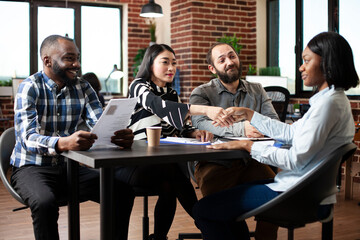 Asian recruiter shakes hands with african american woman, welcoming her to the job interview in modern workspace. Multiethnic HR team begins recruitment meeting with black female candidate.