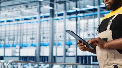Smart factory expert using digital device app to test automated systems and ensure reliability. Worker uses tablet to identify bottlenecks and optimize gear based on sensors data, camera A close up