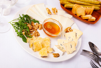 Delicious tasty cheese dish for romantic dinner, assorted cheese with nuts and honey on white plate