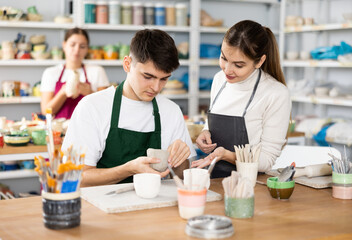 Fototapeta premium Young woman and young man sculpting ceramic product in workshop