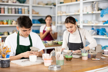 Young woman and young man sculpting ceramic product in workshop