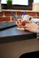 Closeup of business person writing on sticky note on office desk, planning work schedule. Selective...