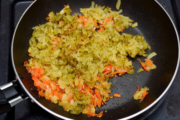 Stewing finely chopped onions with carrots and grated pickled cucumber in a frying pan.