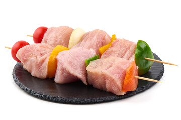 Raw turkey skewers with vegetables on a black slate plate, isolated on white background.