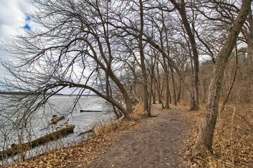 Early Spring landscape of a hiking trail alongside the Illinois River under a partly cloudy sky at Starved Rock State Park near Oglesby, Illinois.