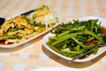 Close-up of Thai dishes of stir-fried morning glory (Kang Kong) and red curry chicken on a table with gingham tablecloth at Cliff Restaurant, Patok Bay - Koh Racha, Thailand
