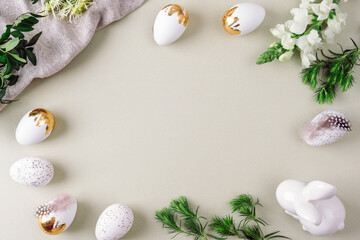 White and golden Easter eggs, Easter Bunny, feathers and greenery on soft background. Top view, flat lay, copy space