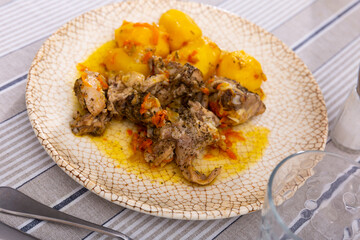 Stewed chicken pieces with sliced potato and vegetables served in a plate with other table appointments