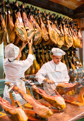 Young couple work together in butcher shop - they cut the traditional Spanish jamon