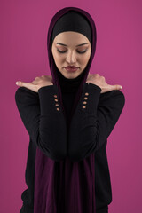 Fototapeta premium Beautiful Muslim woman in a hijab posing elegantly in a studio with a pink background.