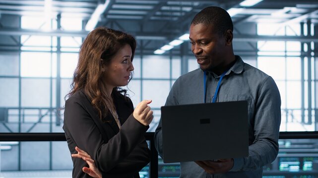 Engineers using laptop in data center, managing server virtualization, running scripts. IT specialists using programming language on notebook in server hub, finetuning network protocols, camera A