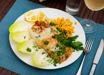 Appetizing fried rockling fillet with garnish of boiled corn seeds, lemon slices and fresh greens