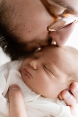 Loving father carying of his newborn baby at home. Bright portrait of happy man holding cute infant child on hands. Dad hugging his little 1 months old son