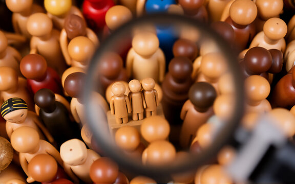 A magnifying glass focuses on a group of wooden figures within a larger diverse collection.  The scene emphasizes scrutiny, selection, and observation.