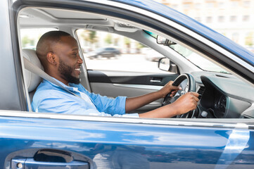 Happy Driver. Side view profile portrait of cheerful positive African American man sitting in a car on driver's seat. Excited black guy riding in the city, holding hands on steering wheel © Prostock-studio