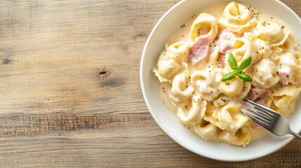 A creamy plate of tortellini garnished with fresh mint, served on a rustic wooden table.