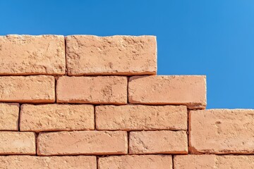 Obraz premium A close-up of a brick wall against a clear blue sky, showcasing textured terracotta bricks stacked in a staggered pattern.
