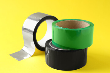 Rolls of different adhesive tapes on yellow background, closeup