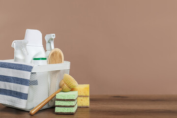 Eco-friendly cleaning products and supplies in basket on wooden table against beige background,...