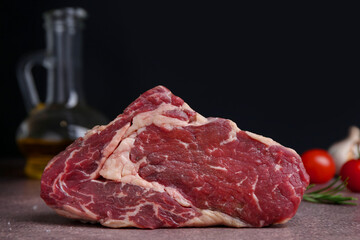 One piece of raw beef on brown textured table against black background, closeup