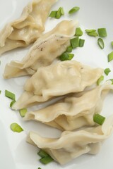 Tasty boiled gyoza (dumplings) with green onion on plate, top view