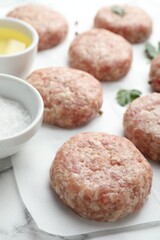 Many uncooked patties, salt, oil and parsley on white table, closeup