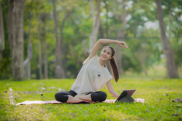 A enthusiastic Asian sports woman stopped after exercising at the garden, sitting on a exercise...