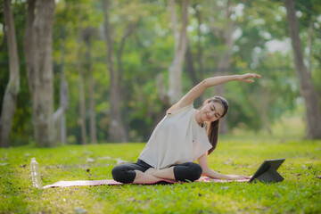 A enthusiastic Asian sports woman stopped after exercising at the garden, sitting on a exercise...