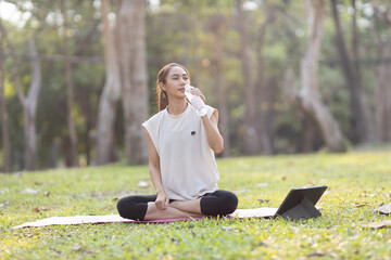 A enthusiastic Asian sports woman stopped after exercising at the garden, sitting on a exercise...