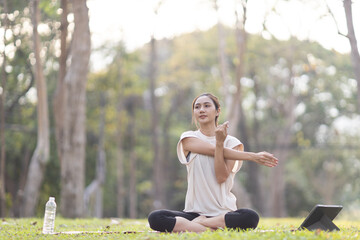 A enthusiastic Asian sports woman stopped after exercising at the garden, sitting on a exercise...