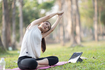A enthusiastic Asian sports woman stopped after exercising at the garden, sitting on a exercise...
