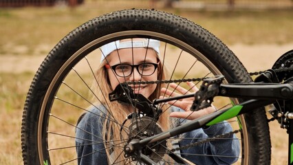 An eleven-year-old girl twists and looks at the wheel of her bicycle.
