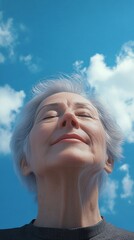 Intimate portrait of an elderly woman with silver hair, exuding tranquility and contentment, in a vertical composition, set against a backdrop of a clear blue sky with scattered fluffy clouds