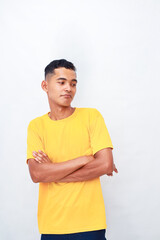 Pensive Asian man in yellow t-shirt with crossed arms on white background