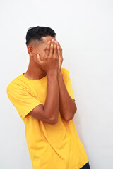 Asian man with a bright yellow t-shirt covering his face in distress