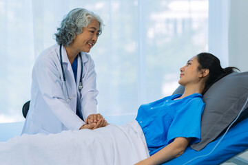 Obraz premium An elderly Asian female doctor is writing on a clipboard with a young female patient in a hospital room.