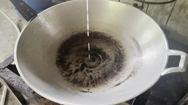 Asian cook is cooking in thai kitchen in local traditional country style, preparing  pouring melted pork lard into a traditional wok to cooking high heat stir frying food