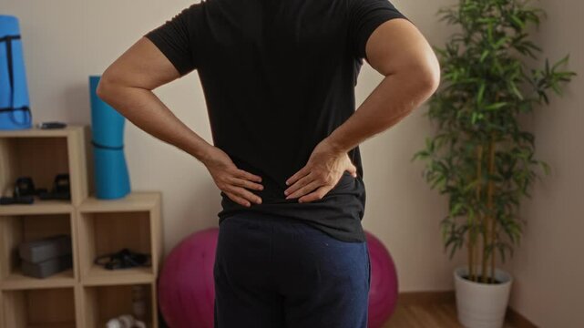 Man standing with hands on back at gym interior with fitness equipment in room showcasing active lifestyle and exercise setting indoors.