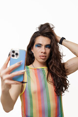 Genderqueer person takes a selfie wearing pride clothing, smiling and posing happily for the camera.