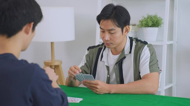 Asian young men poker players playing casino card game together in house.