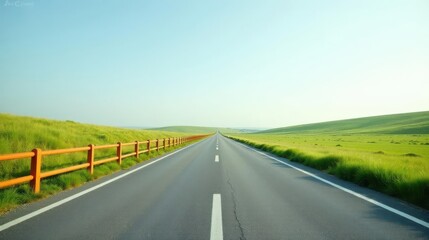 Fototapeta premium Endless asphalt road lined with a vibrant orange fence, disappearing into a serene, gently rolling green landscape under a clear sky